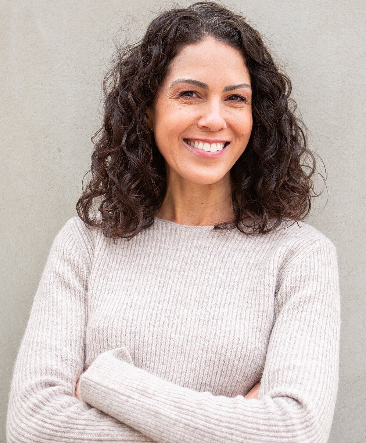 Smiling woman with curly hair in beige sweater.