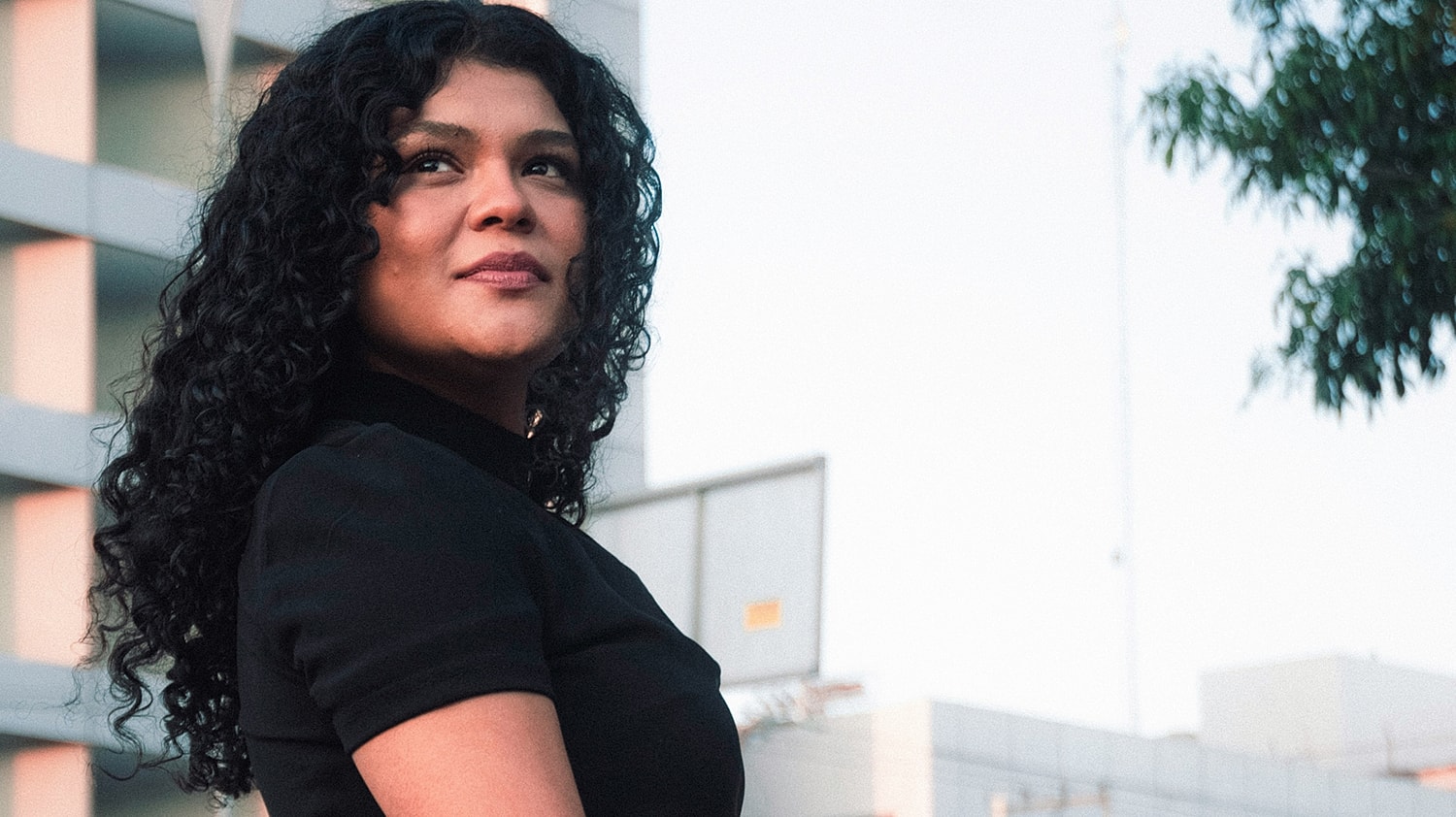 Woman with curly hair against urban backdrop.