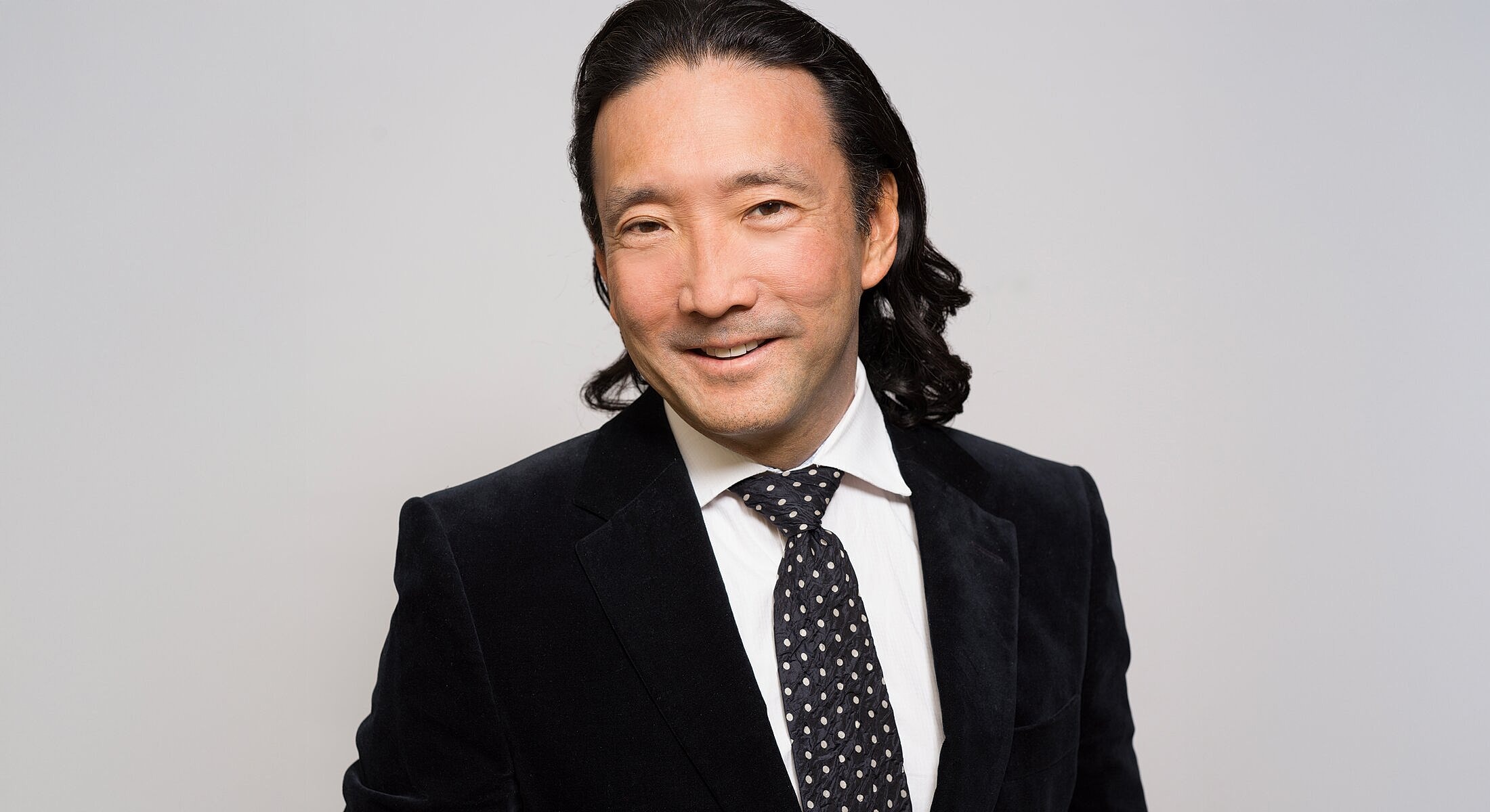 Man smiling in formal attire against neutral background.