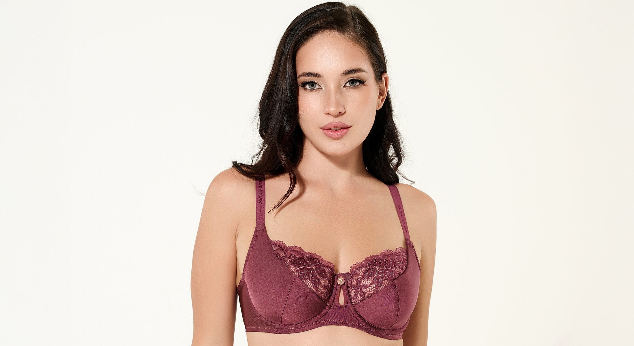Model wearing burgundy lace bra on white background.