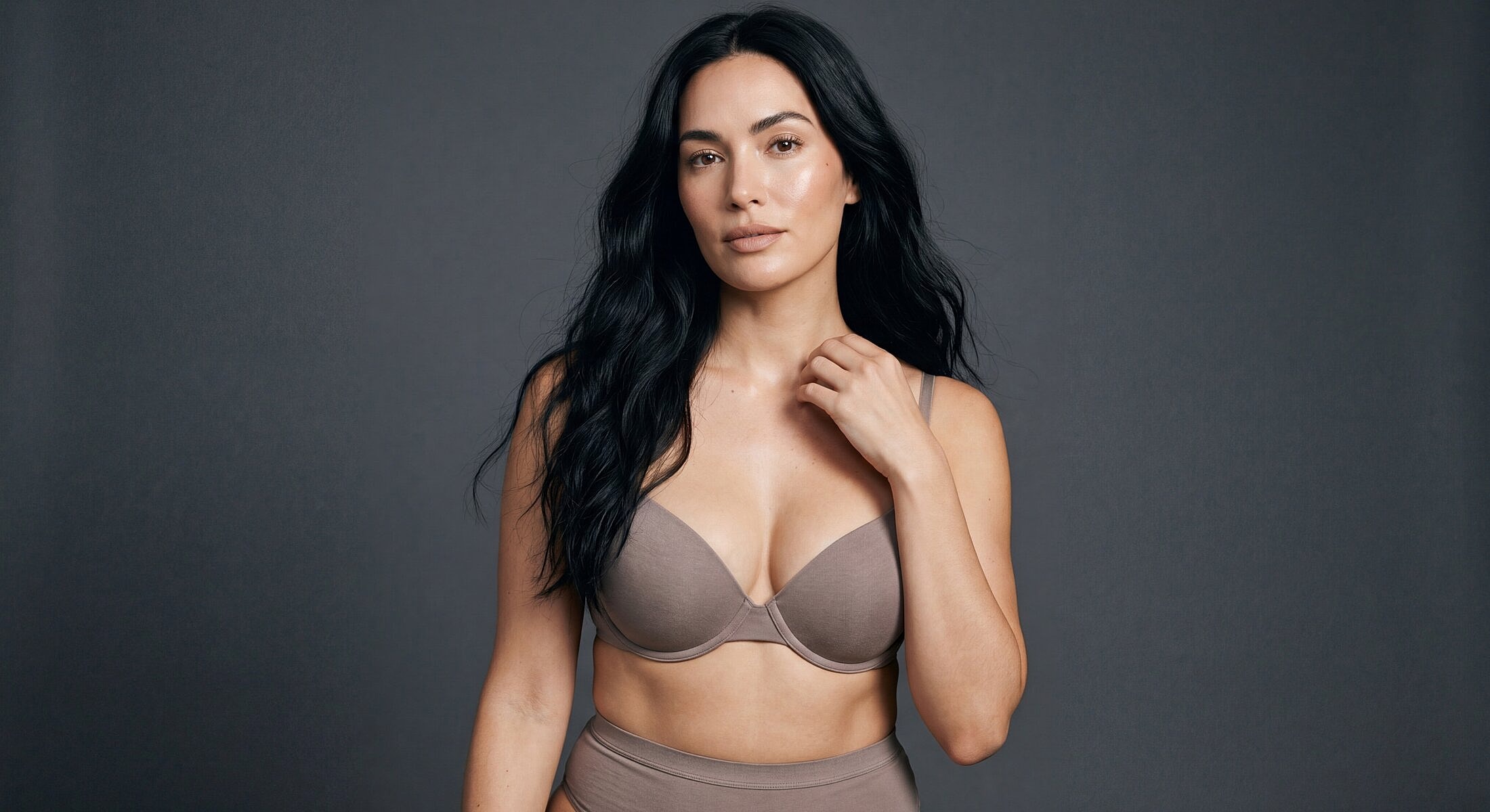 Woman in neutral lingerie against dark background.